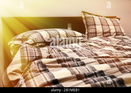 El sol brilla a través de la ventana del dormitorio. Las mantas y almohadas no hechas no están escondidas Foto de stock