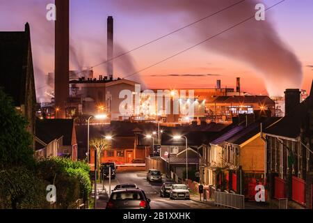 Viviendas residenciales que conducen a las obras de acero de Port Talbot emitiendo nubes de vapor en la luz de la noche Port Talbot Swansea Glamourgan Wales Foto de stock