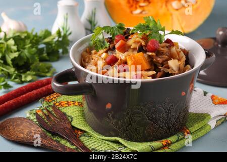 Estofado de verduras con salchichas de caza en una olla de cerámica sobre un fondo azul claro Foto de stock