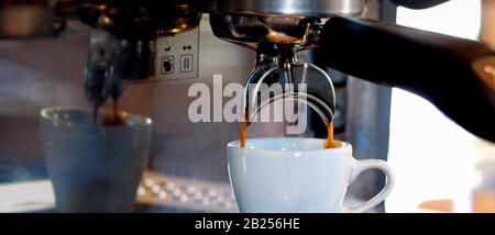 Un banner de tamaño ordenador muestra el espresso goteando en una taza blanca de una cafetera espresso. Foto de stock