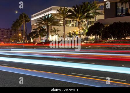 Coloridos senderos de luz en una carretera de la ciudad frente a edificios iluminados por la noche.