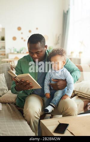 Retrato vertical de un hombre africano-americano maduro leyendo un libro al niño sentado en el regazo de los padres