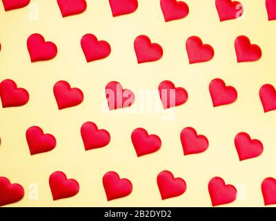 Muchos corazones de seda roja idénticos que se encuentran escalonados sobre un fondo amarillo. Símbolo de amor, ternura y pasión.