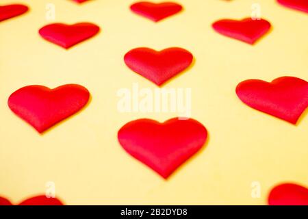 Muchos corazones de seda roja idénticos que se encuentran escalonados sobre un fondo amarillo. Símbolo de amor, ternura y pasión.