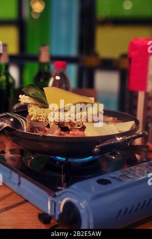 Plato crudo asiático cocinado en un horno de gas fijo - fosos liofilizados, una rebanada de queso y carne en el proceso de cocción Foto de stock