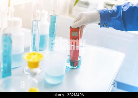 Análisis de la calidad del agua en un laboratorio químico, un dispositivo para medir el pH con equipo de vidrio, las manos de un científico con un pH rojo Met Foto de stock