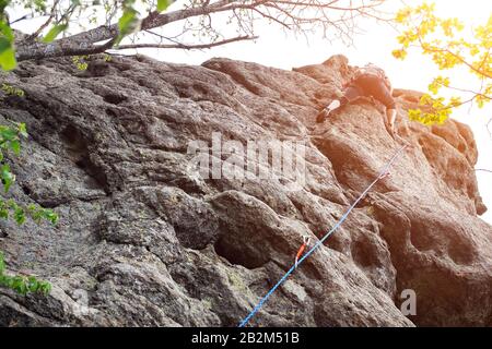 Escalador masculino, escalador joven escalando una ruta difícil en un acantilado. El escalador sube a una pared rocosa. Con cuerda de seguridad en la roca. Superar obstáculos Foto de stock