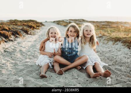 Retrato de tres hermanas jóvenes abrazando y sonriendo en arena