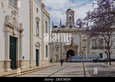 El tren turístico recorre el arco de la ciudad, Arco da Vila en Faro, Portugal. El arco neoclásico fue construido en 1812 en el sitio de una puerta medieval Foto de stock