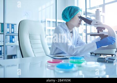 Inyección horizontal de una científica médica asiática que trabaja en un laboratorio moderno utilizando un microscopio y un espacio de copiado