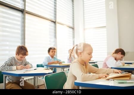 Foto horizontal de jóvenes estudiantes de escuela intermedia sentados en escritorios en un salón de clase moderno que tienen espacio para clases y copias