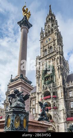 La imponente columna de la Mariensäule contra la ricamente decorada fachada del Nuevo Ayuntamiento de Munich (Neues Rathaus) con su Rathausturm de 85 m de altura Foto de stock