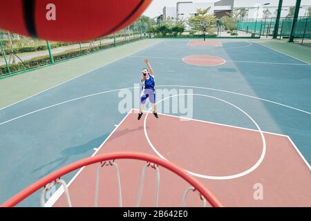Jugador profesional femenino de baloncesto lanzando pelota en la cesta cuando jugando en la cancha al aire libre