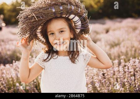 Pequeña chica caucásica posando alegremente en el campo de lavanda con una corona de flores en la cabeza