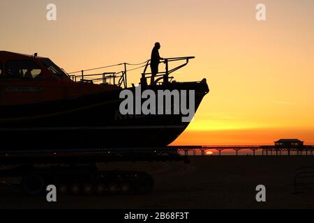 El salvavidas de St annes es guiado a casa en el resplandor de un cielo naranja mientras el sol se pone entre los arcos del muelle victoriano Foto de stock