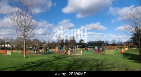 Los niños disfrutan de las áreas de juego en Salt Hill Park, Slough, mientras sus padres miran. Día soleado. Finales del invierno. Foto de stock