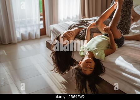 madre y niña acostada en la cama divirtiéndose juntos Foto de stock
