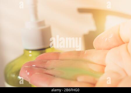 Mano femenina usando jabón líquido de un dispensador. Limpiador verde en los dedos