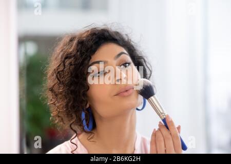 Mujer de cabello oscuro aplicando polvo en su cara Foto de stock