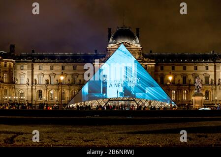 Una presentación ligera exhibida en una pirámide de cristal en la entrada del museo del Louvre por la noche, París, Francia