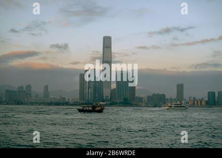 Perfil de Hong Kong al atardecer con barcos que pasan por el río