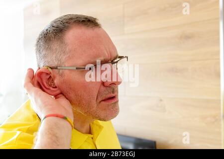 Hombre llevando ayuda en oídos sordos intenta escuchar algo Foto de stock