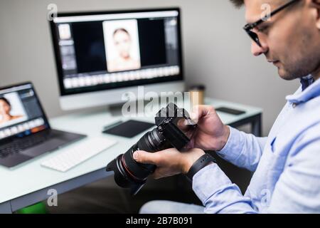 Guapo fotógrafo sosteniendo su cámara sonriendo a la cámara en la oficina creativa