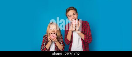 Hermanos preadolescentes hermano y hermana comiendo donuts, posando sobre fondo azul Foto de stock