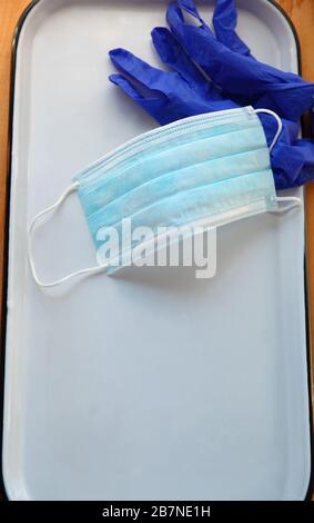 Mascarilla facial y guantes de plástico en una bandeja blanca con espacio para copias Foto de stock