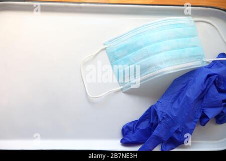 Guantes de plástico y mascarilla facial desechable en una bandeja blanca con espacio para texto Foto de stock