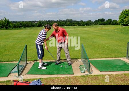 Un instructor de golf para adultos que enseña a un joven adolescente golfista la técnica de posicionamiento y manejo del club de golf en el campo de prácticas. Foto de stock