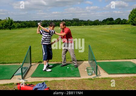 Un instructor de golf para adultos que enseña a un joven adolescente golfista la técnica de posicionamiento y manejo del club de golf en el campo de prácticas. Foto de stock