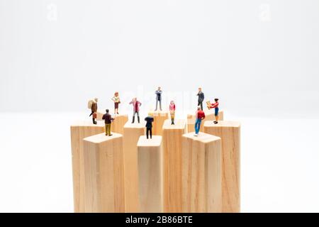 Juguetes en miniatura de pie sobre bloque de madera - concepto de distanciamiento social, antisocial o de trabajo en equipo.