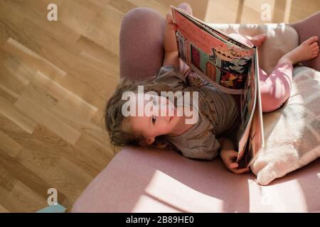 vista areal de una niña mirando hacia arriba leyendo sentada en una silla en casa Foto de stock