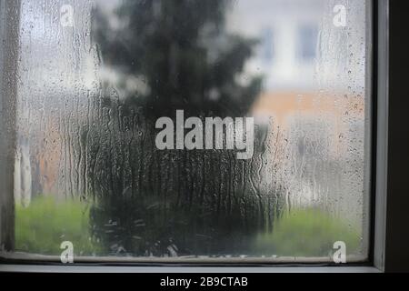 ventana empapada por tormenta de lluvia. gotita de agua atrapada en una ventana de cristal transparente. imagen borrosa de la casa al otro lado de la calle Foto de stock