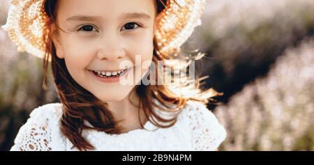 Chica pequeña caucásica posando con un sombrero en un campo de lavanda mientras mira la cámara