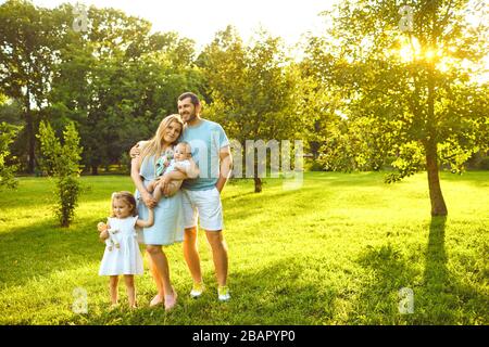 Los padres con el bebé están de pie sobre la hierba en el parque Foto de stock