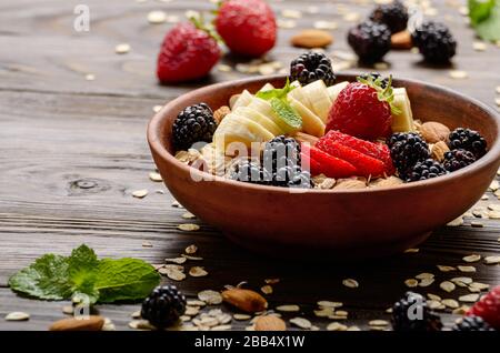 Muesli saludable fruta fresa banana con almendras y blackberry en arcilla plato sobre la mesa de la cocina de madera