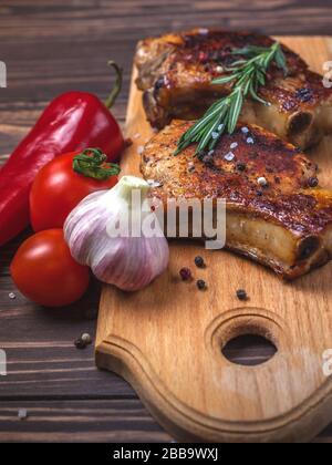Filetes de cerdo a la parrilla y verduras en una mesa rústica de madera. Carne a la parrilla sobre el hueso con especias, ajo, pimientos, tomates y romero. Menú del restaurante Foto de stock
