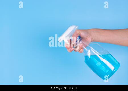 La mano de la mujer sostiene el aerosol del alcohol sobre fondo azul del cielo. Rociar un spray desinfectante antibacteriano, desinfectante de manos para prevenir el Coronavirus o Covid-19.