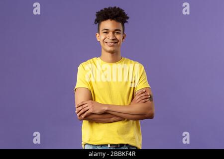 Retrato de primer plano de un joven estudiante profesional, inteligente y seguro con dreadlocks, camiseta amarilla, brazos cruzados sobre el pecho y una sonrisa feliz
