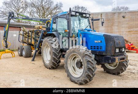 Gran tractor Valtra 6550 finlandés azul con cabina y 4 ruedas grandes con neumáticos, con un remolque lleno de troncos de pino talados, Surrey, sudeste de Inglaterra