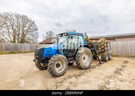 Gran tractor Valtra 6550 finlandés azul con cabina y 4 ruedas grandes con neumáticos, con un remolque lleno de troncos de pino talados, Surrey, sudeste de Inglaterra
