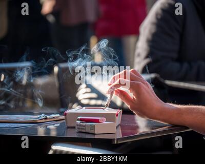 Mujer mano sosteniendo el cigarrillo con humo en la mesa. Fumar adicción a la nicotina estilo de vida malsano.