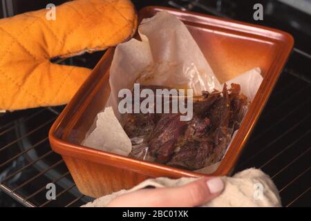 La carne de pato se cuece en el horno sobre una placa de cerámica. Las manos de una niña pusieron la cocción dentro del horno. Foto de stock