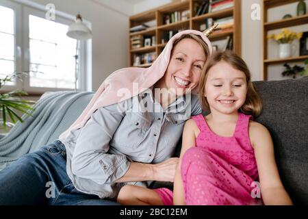 Retrato de feliz madre y su hija pequeña sentados juntos en el sofá divirtiéndose