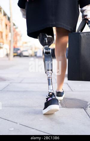 Sección baja de la mujer con prótesis de pierna caminando por la ciudad