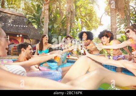 Amigos entusiastas bebiendo, tostar botellas de cerveza y cócteles en la fiesta de verano en la piscina Foto de stock