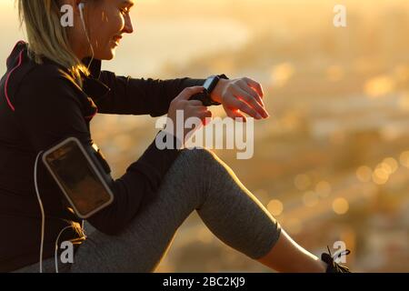 Primer plano de un corredor que lleva tapones para los oídos para comprobar la música en smartwatch sentado al atardecer tras el deporte Foto de stock