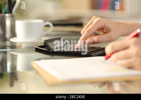 Primer plano de las manos de la mujer contabilidad con calculadora tomando notas sentado en un escritorio en casa Foto de stock